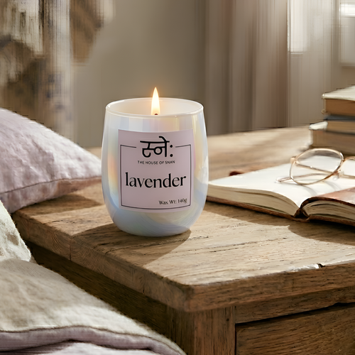Lavender scented candle on a wooden surface with books and glasses in the background