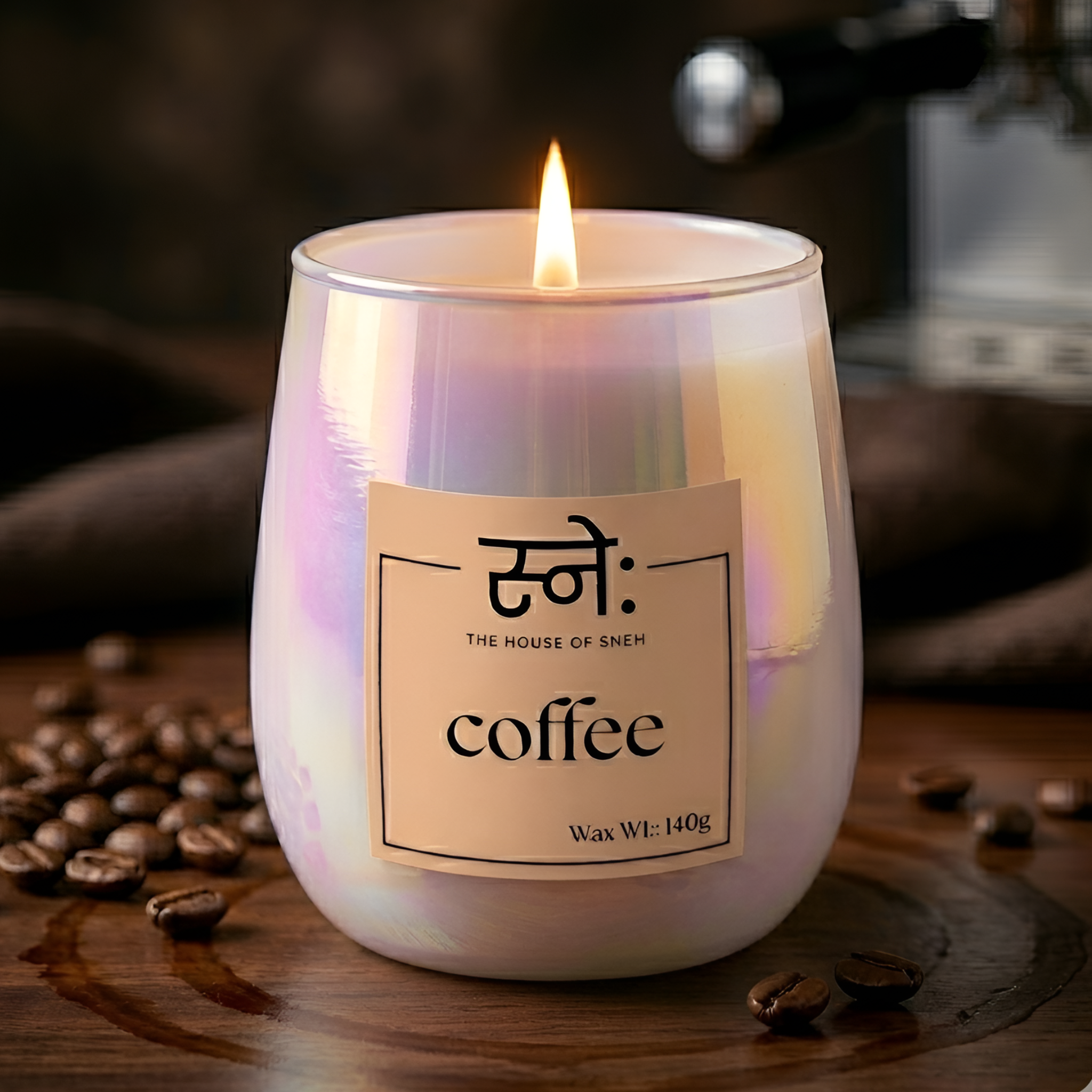 Candle labeled 'coffee' from 'The House of Sneh' with coffee beans around on a wooden surface.